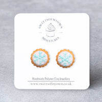 Thumbnail for Pair of cookie-shaped earrings with white icing and blue snowflake on a Sweetsofmyown card against a gray background