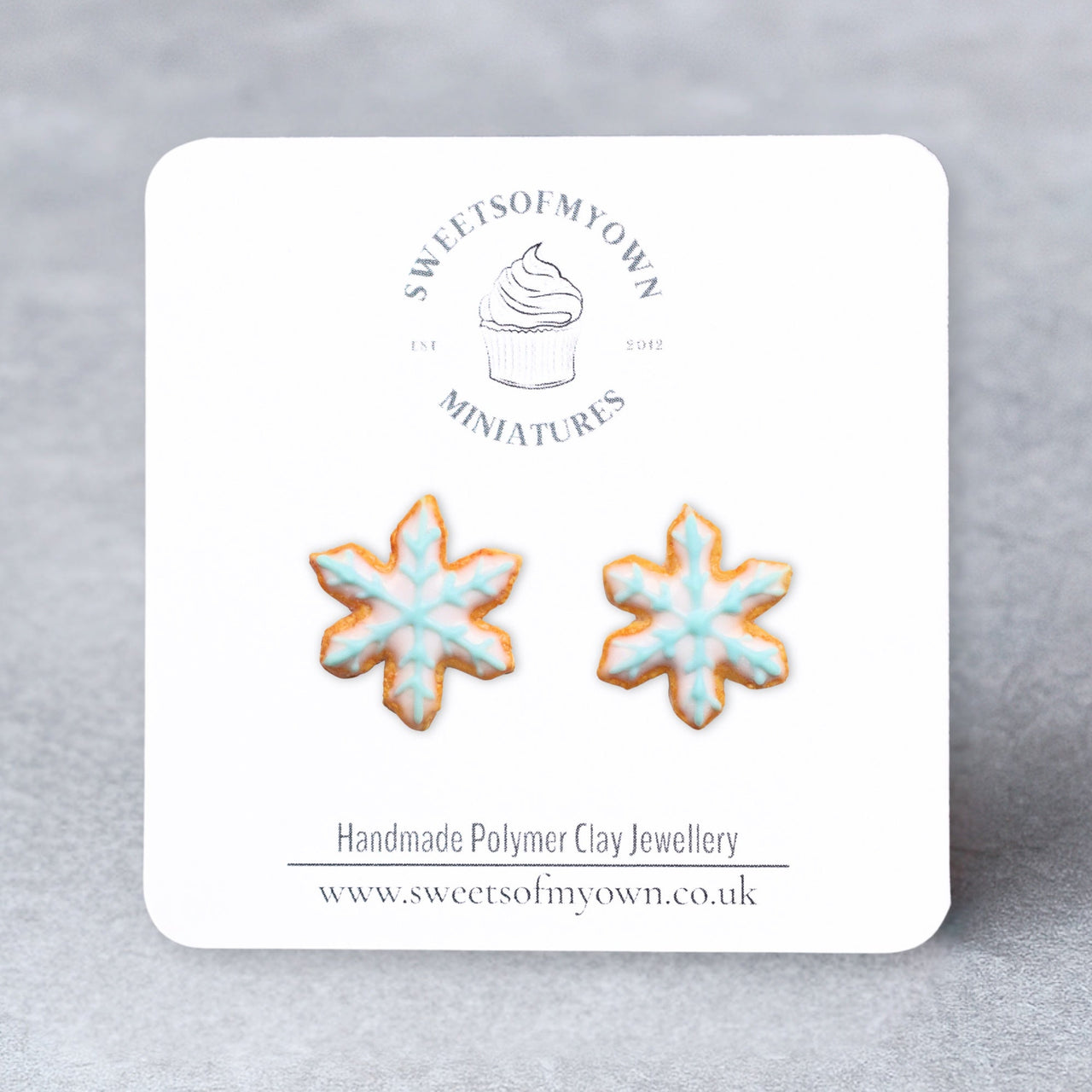 Snowflake-shaped earrings on a branded card with a gray background