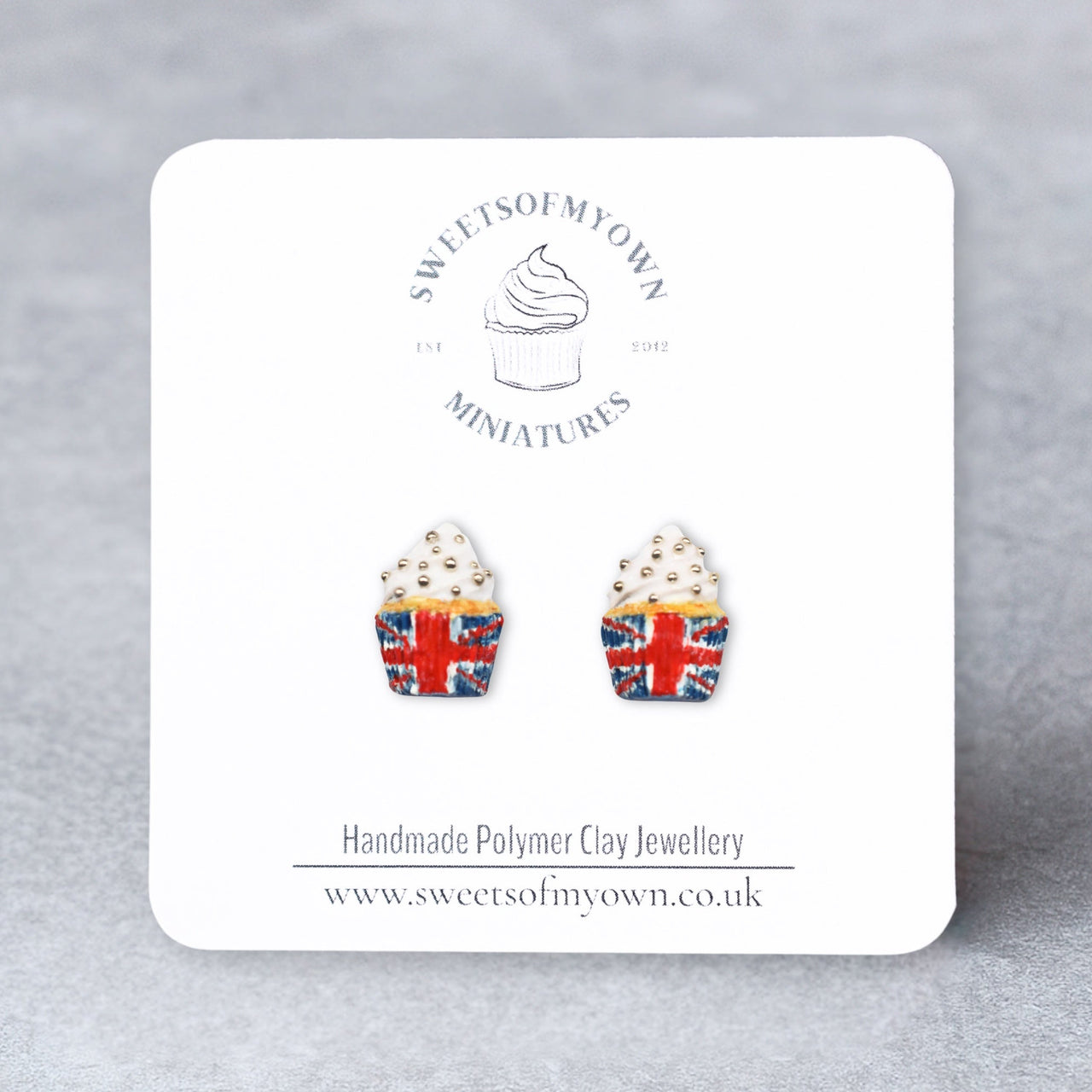 Cupcake-shaped earrings with Union Jack design on a branded card against a gray background